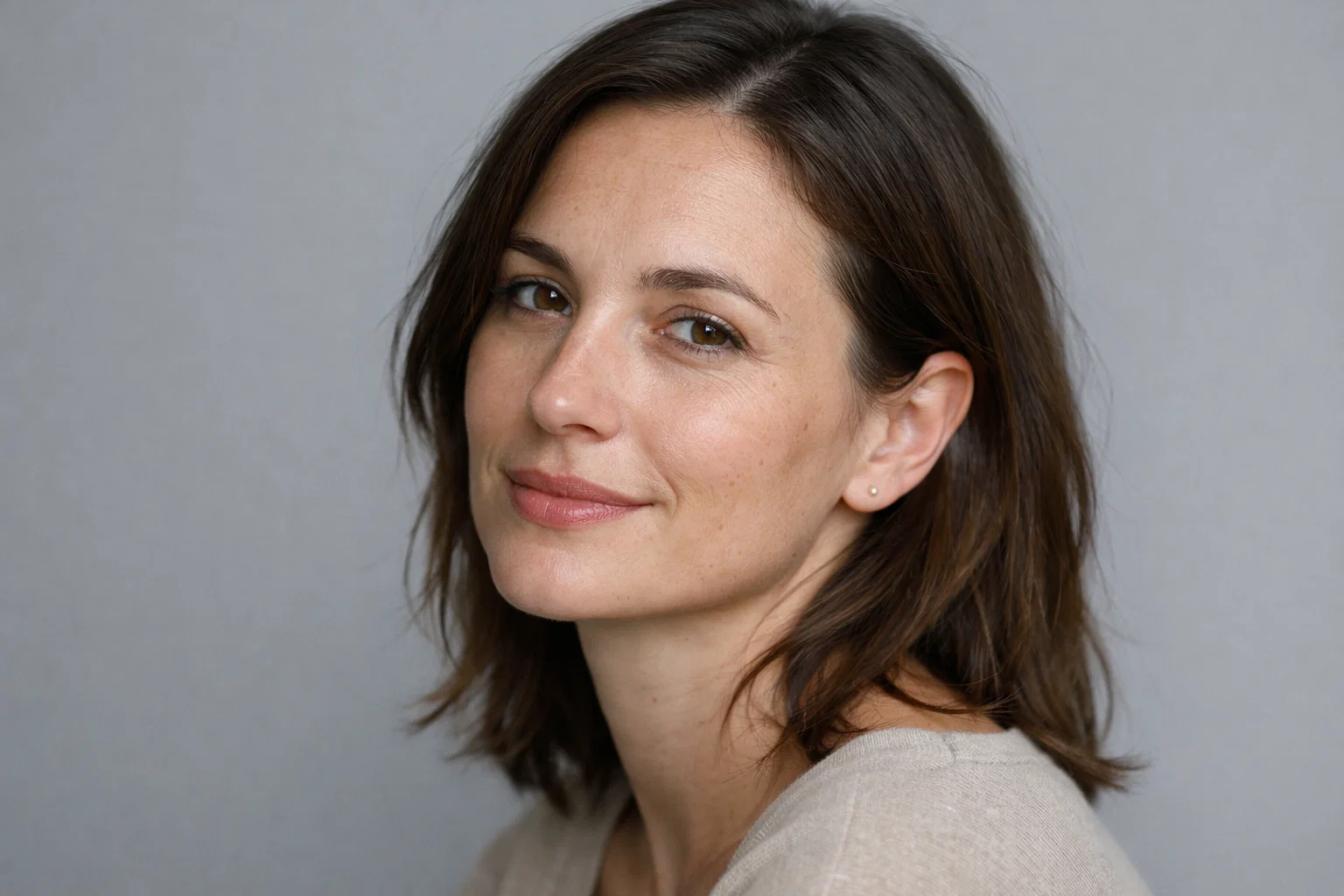 A woman in her thirties with a peaceful expression posing against a soft grey background.