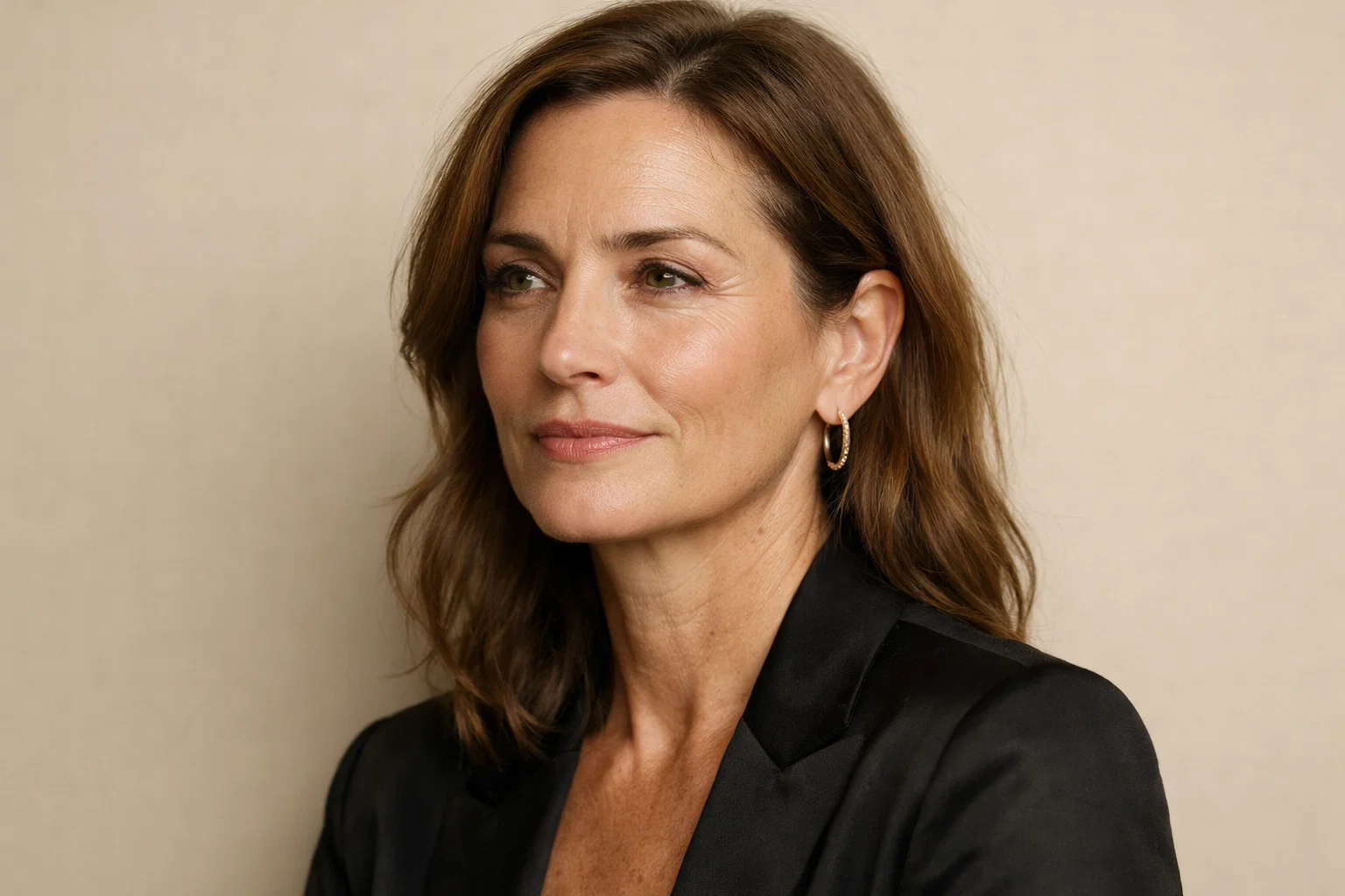 Portrait of an elegant woman showing natural aging signs and facial character on a soft beige background.