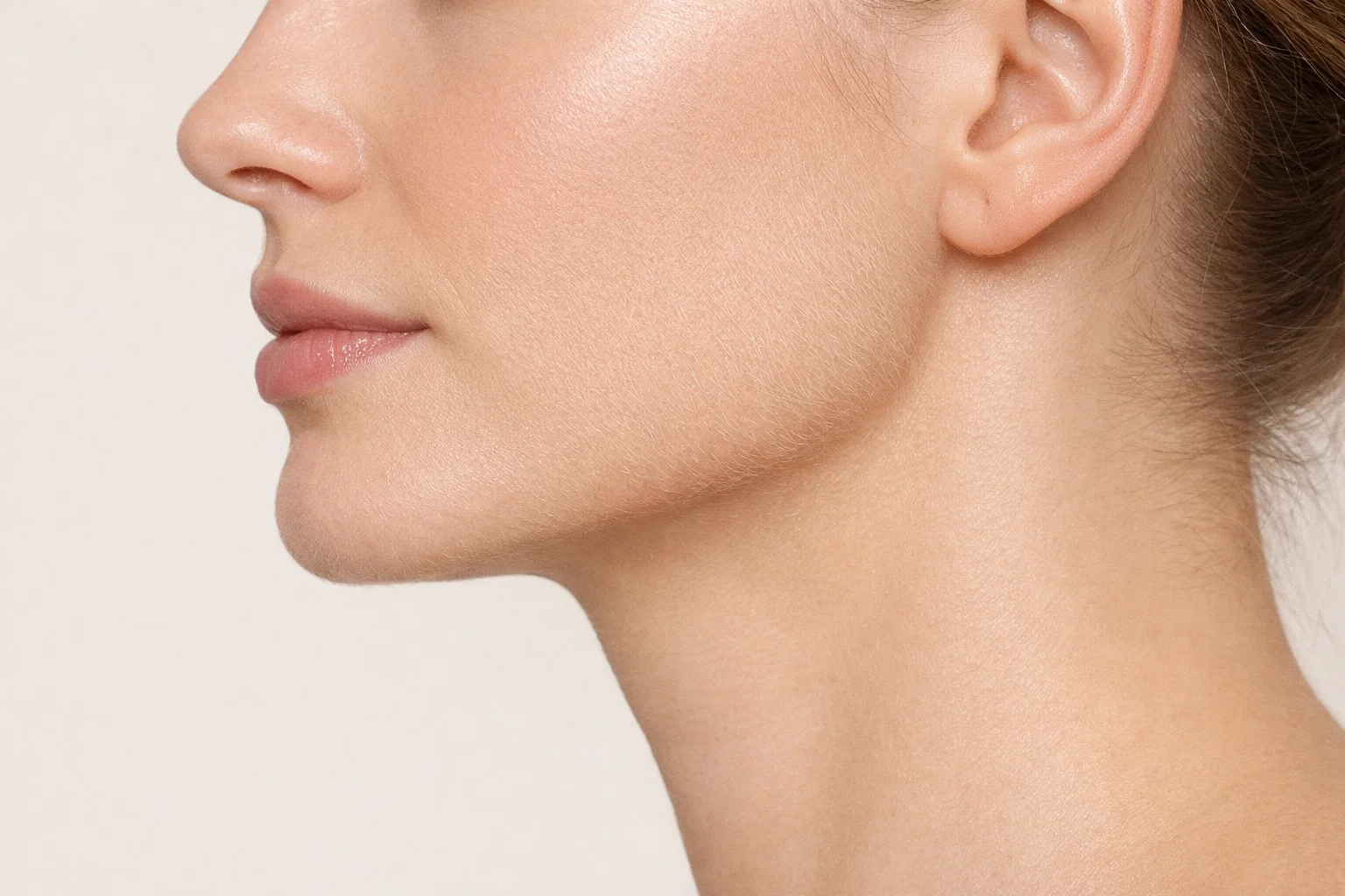 Close-up of a woman's profile against a beige background showing natural skin and fine vellus growth.