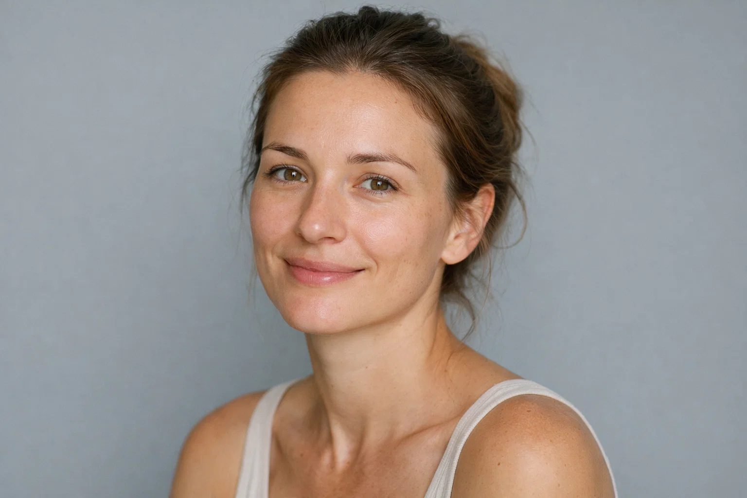 Portrait of a woman with a natural look and gentle smile against a calming soft-grey background.