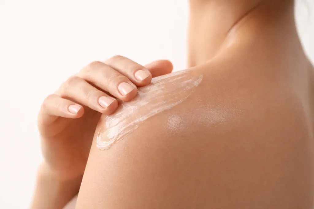 Applying a clear topical gel to a healthy shoulder area against a clean white-beige background.