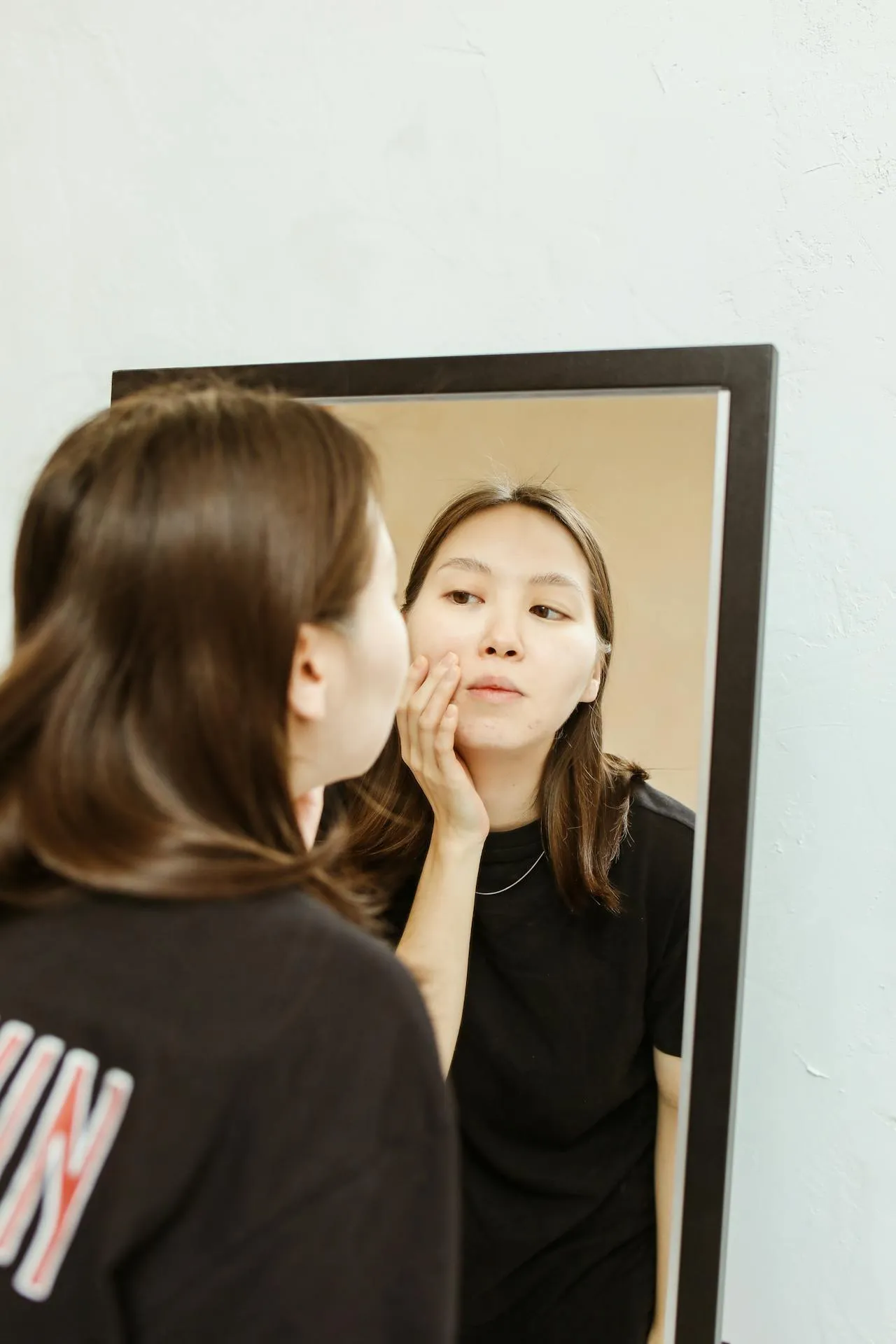 Woman looking in the mirror after non-surgical rhinoplasty treatment with a smooth and balanced nasal profile.