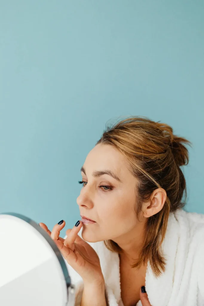 Woman examining early fine lines in a mirror while considering preventative Baby Botox treatment